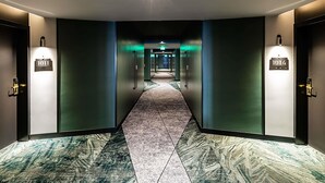 A hotel hallway with a carpeted floor, two doors with illuminated room numbers, and a bright light source at the end. - Novotel Lisboa (Lisbon)