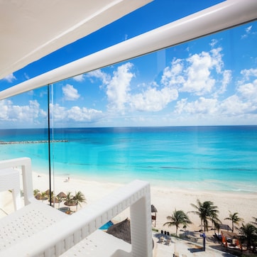 A beach view from a balcony with white wicker furniture and a clear blue sky.