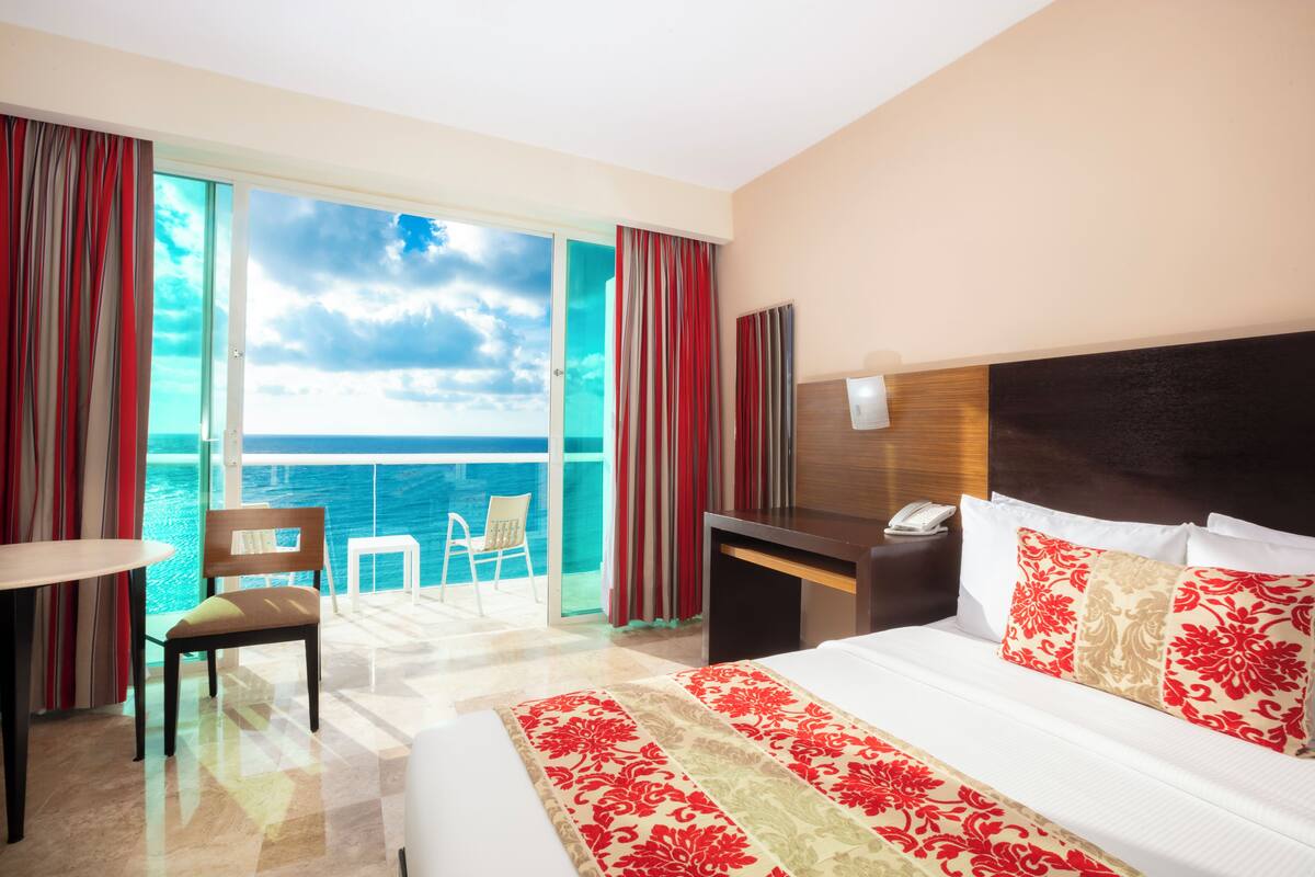 Habitación de hotel con una cama grande, un escritorio, una silla y vista al océano.