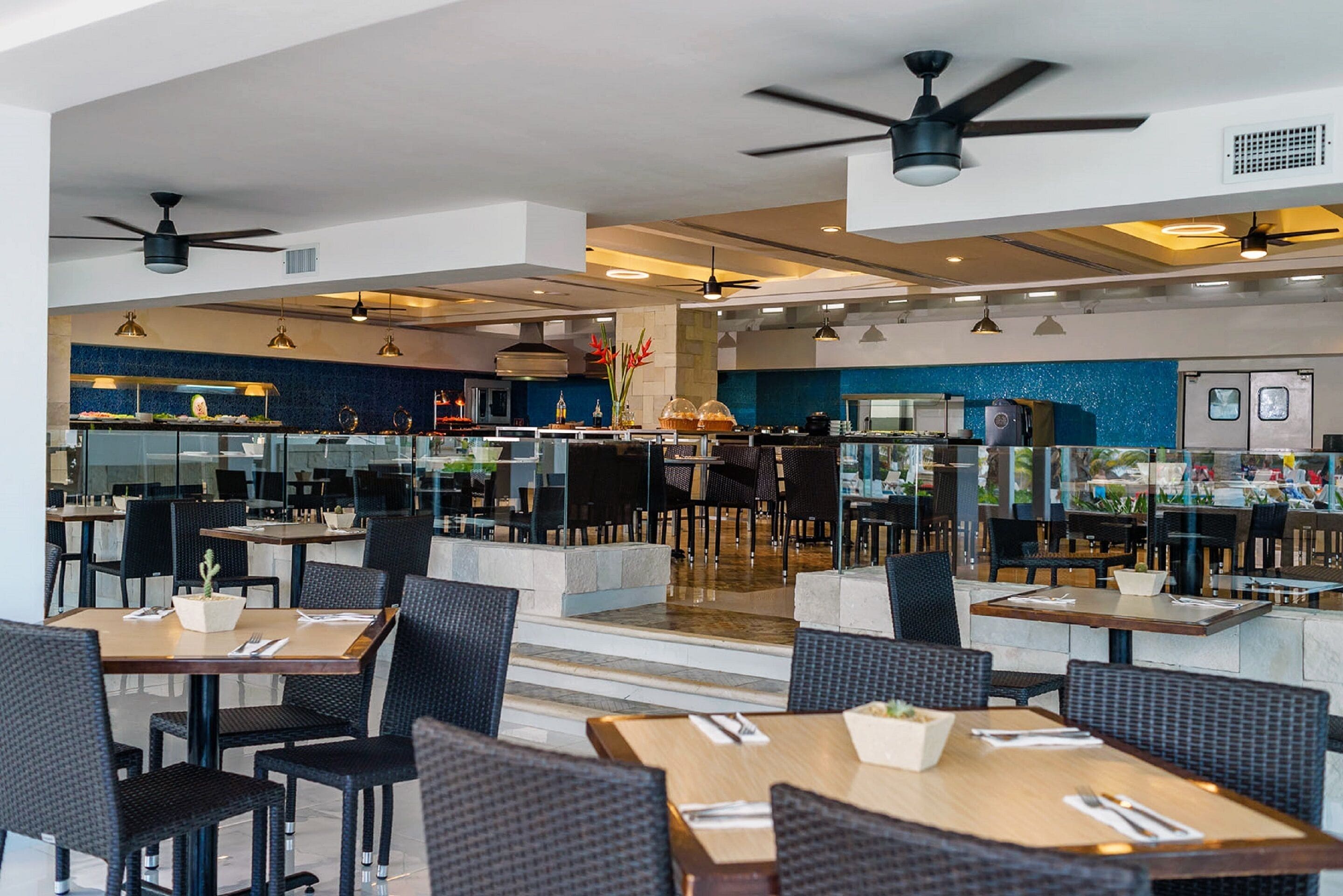 A modern restaurant with multiple dining areas, ceiling fans, and a blue accent wall.