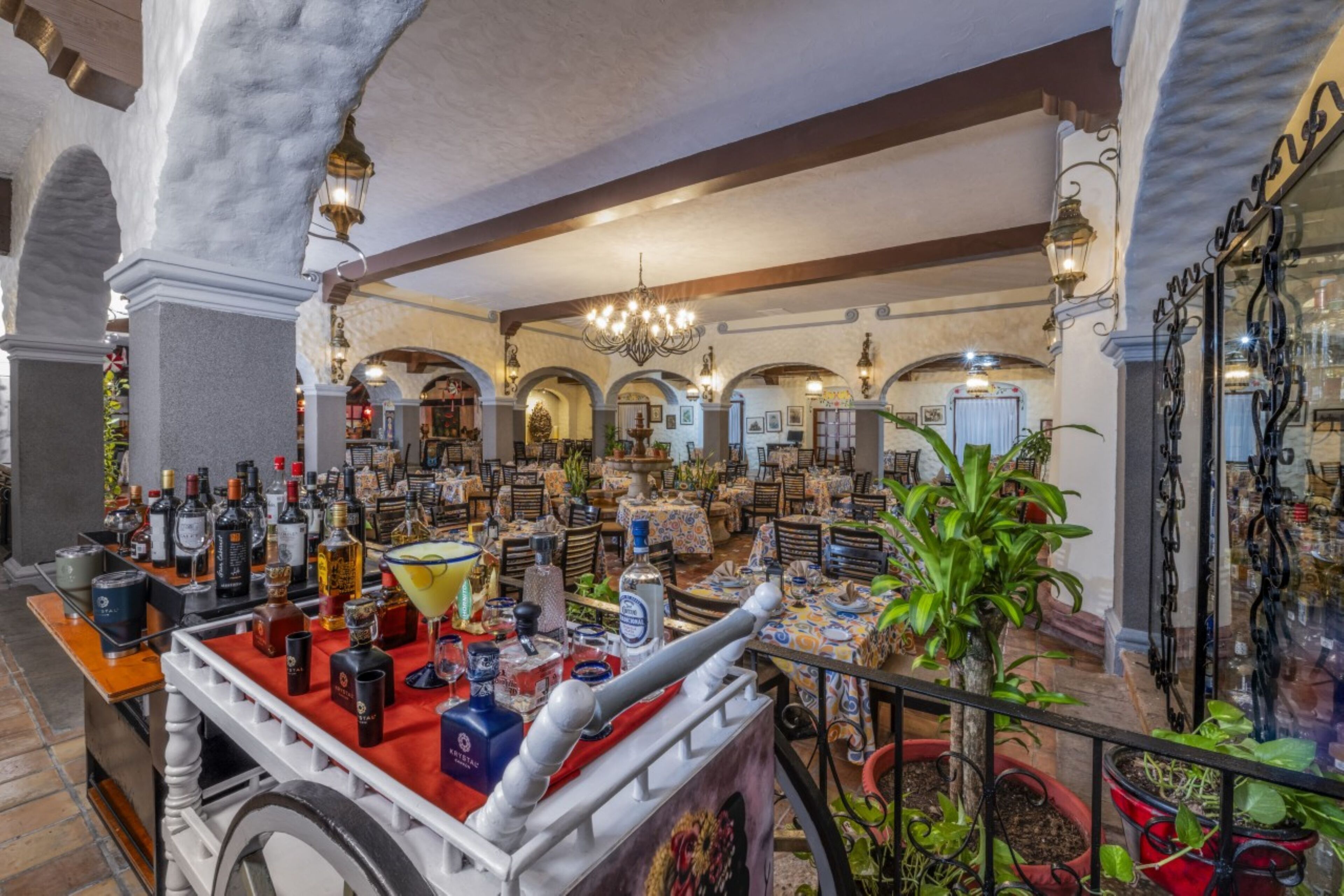 Una zona de bar con varias mesas, una variedad de botellas y un carrito decorativo.