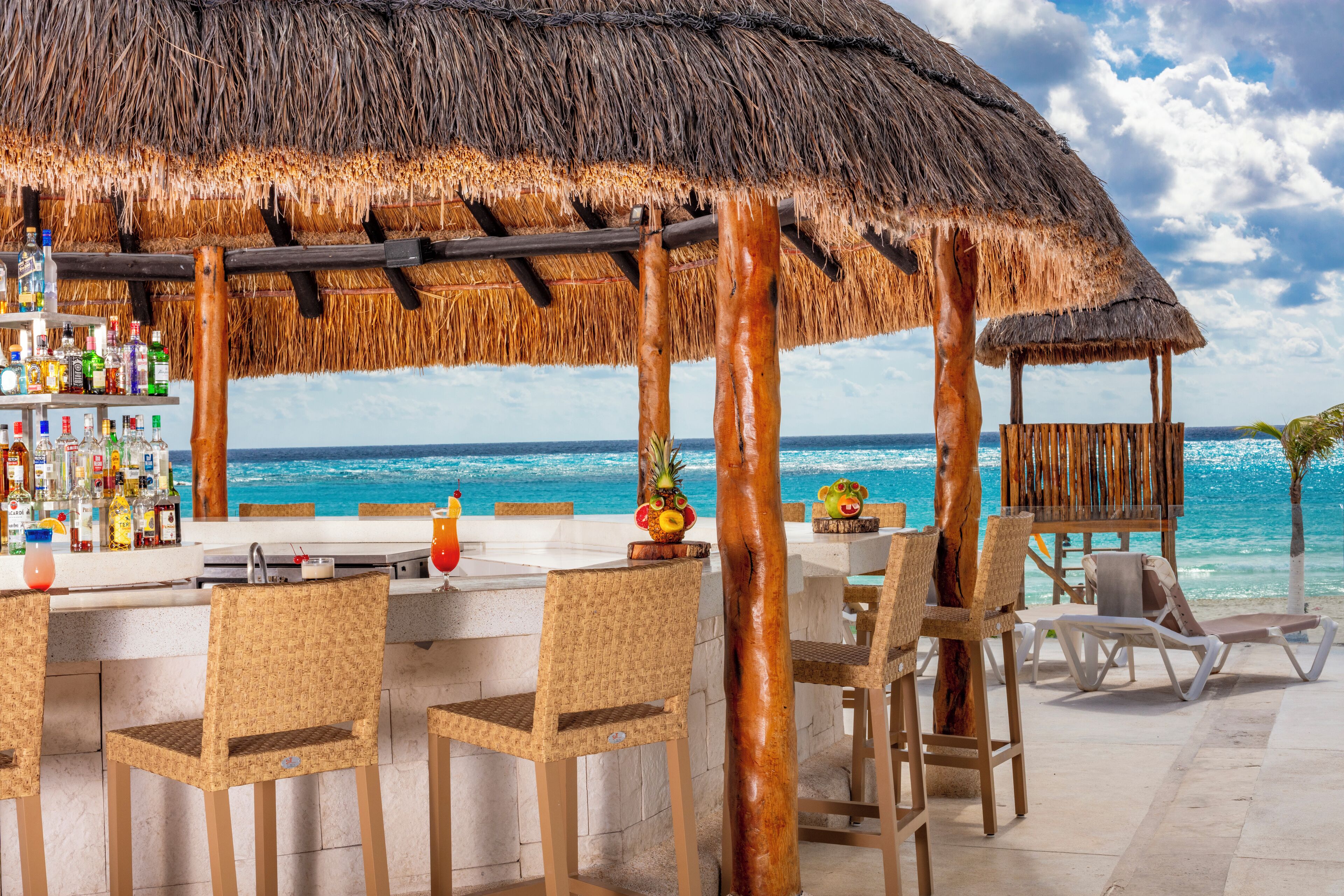 Un bar en la playa con techo de paja, sillas de mimbre y vista al océano.