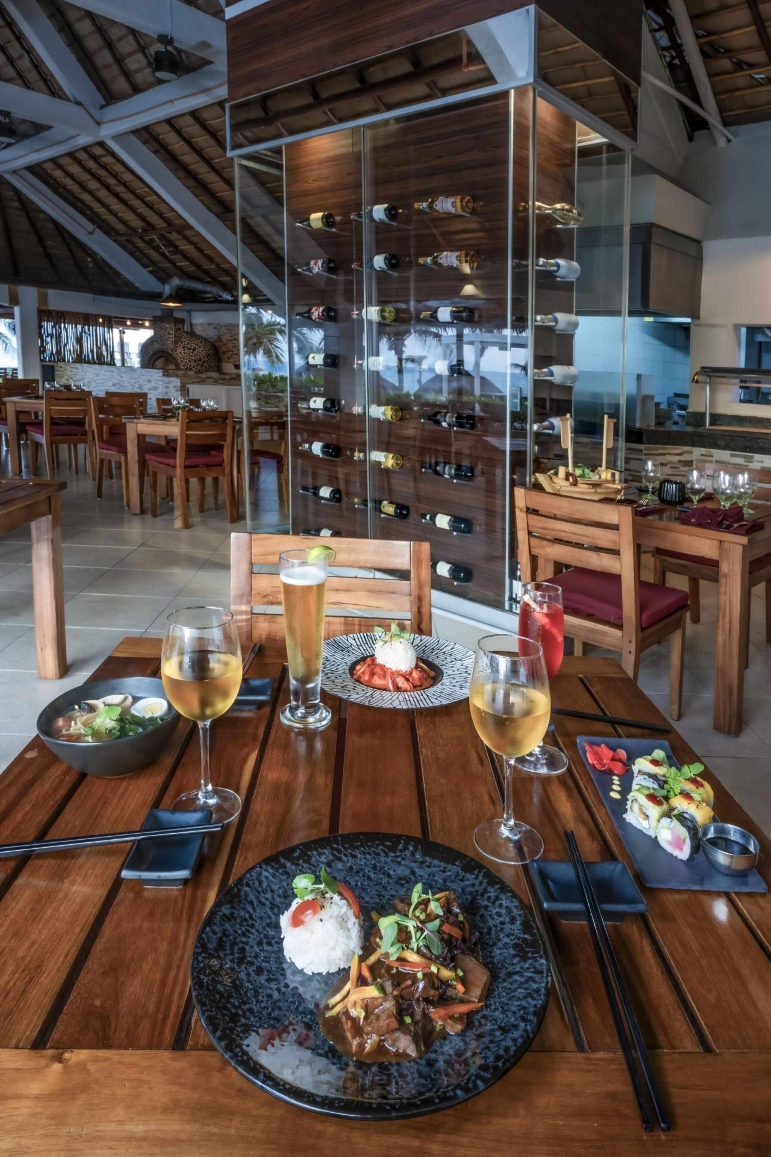 A restaurant with wooden tables, a wine rack, and a variety of dishes including sushi and a bowl of vegetables.