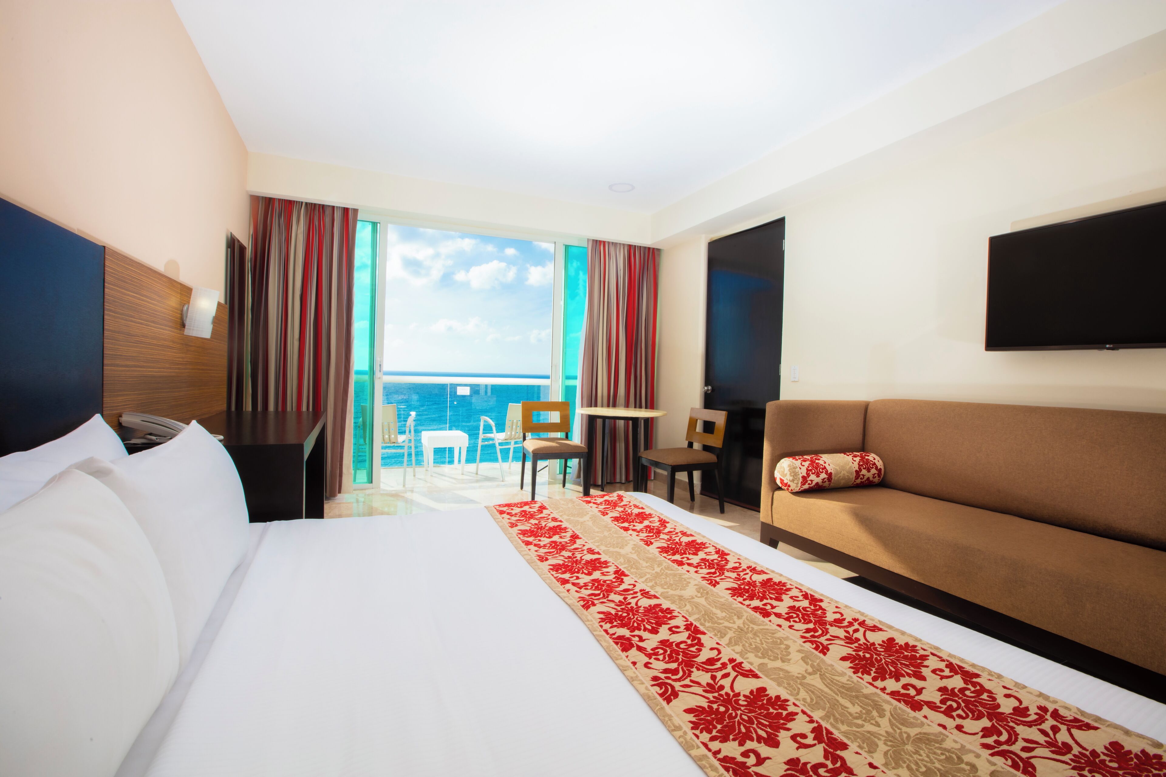 Een hotelkamer met een groot bed, een bank, een televisie, een bureau en uitzicht op de oceaan.
