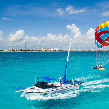 A speedboat with a parasail and a person parasailing over turquoise water.