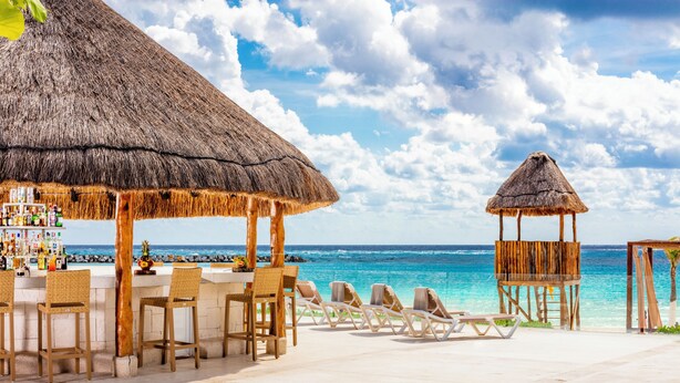 A beachside bar with thatched roofs, lounge chairs, and a view of the ocean.
