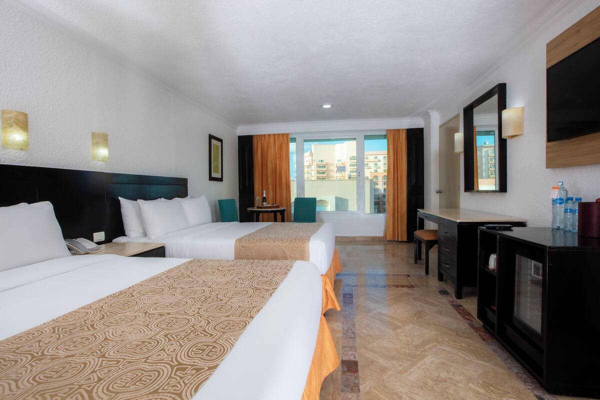 Una habitación de hotel con dos camas, un escritorio, un televisor y un balcón con cortinas.