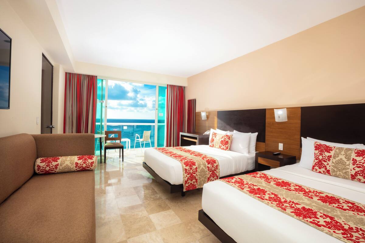 Habitación de hotel con dos camas, un sofá, una silla y vista al océano.