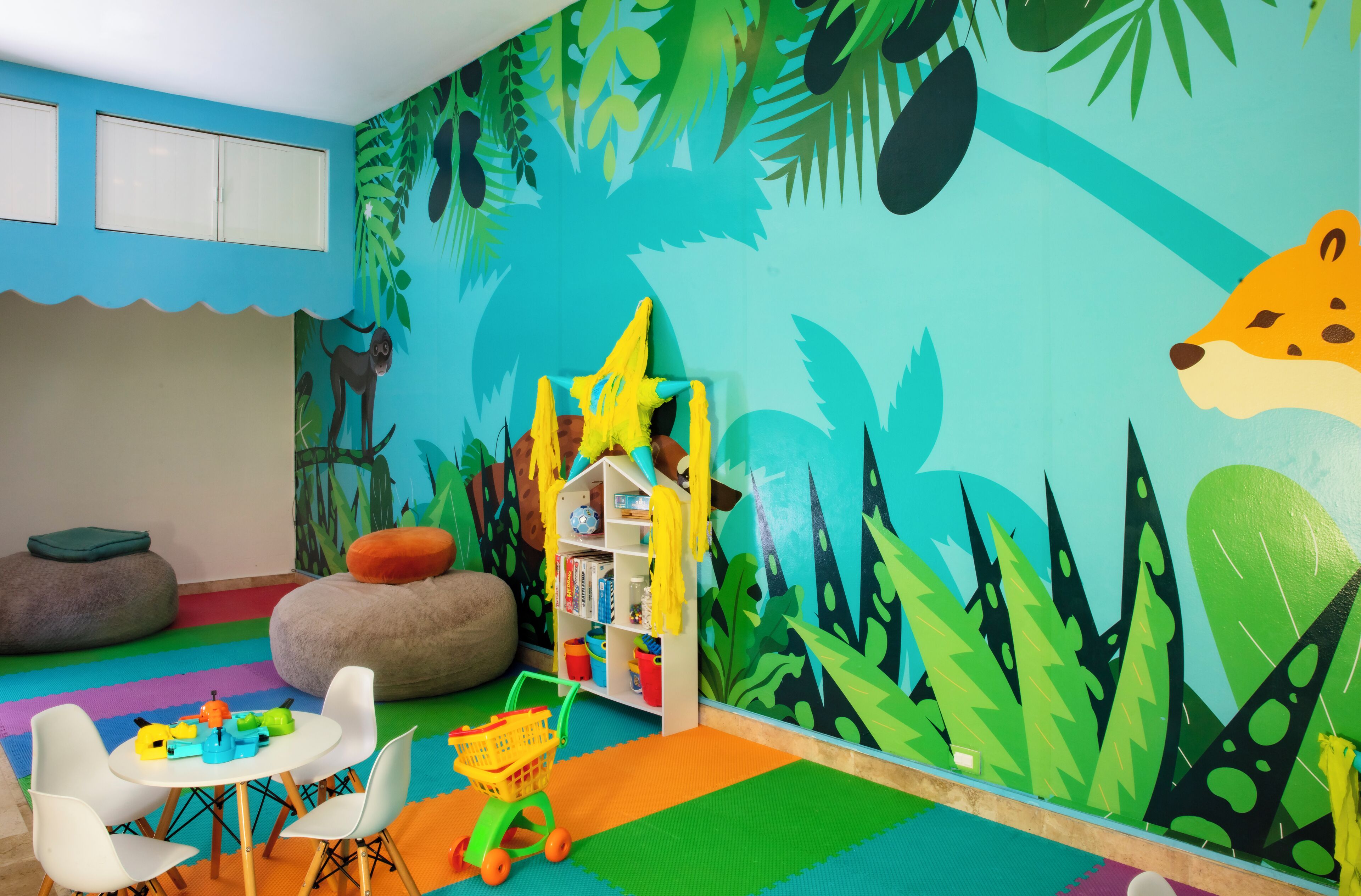 Un salón de juegos infantil vibrante con un mural temático de jungla, una pequeña estantería y coloridos arreglos de asientos.