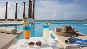 A poolside setting with two drinks, a hat, sunglasses, and a magazine on a lounge chair.