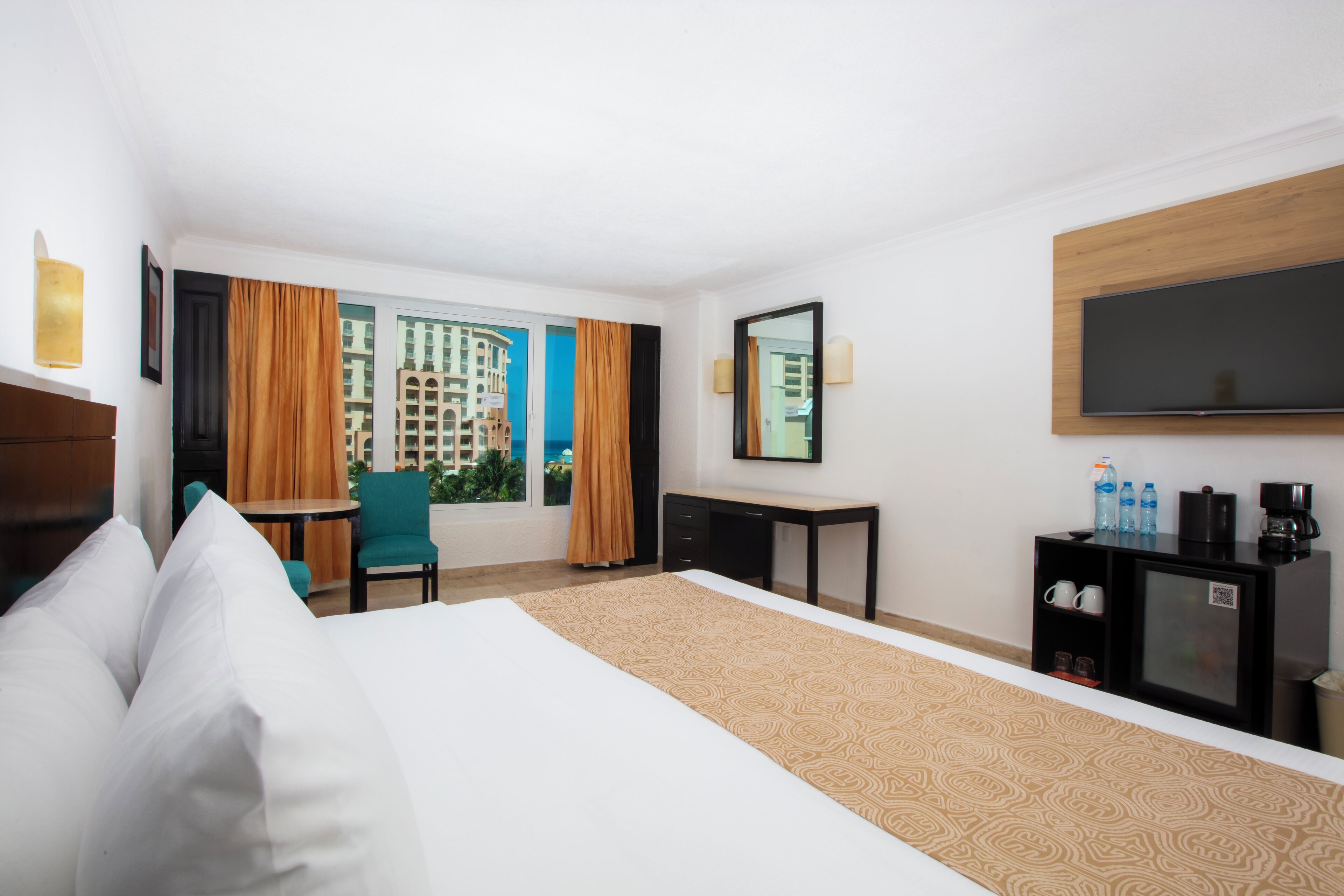 Habitación de hotel con cama, escritorio, silla, televisión y ventana con cortinas.