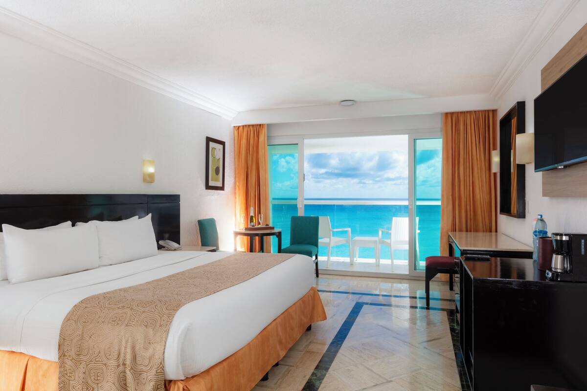 Habitación de hotel con cama, escritorio, silla, televisor y vista al océano.