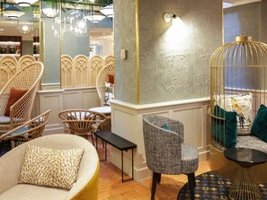 Een kamer met rieten stoelen, een ronde bank, een bijzettafeltje en een decoratieve vogelkooi.