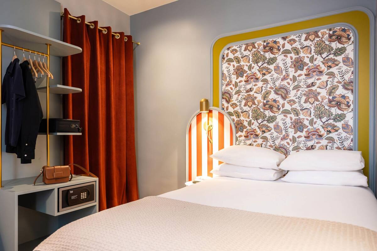 Une chambre d’hôtel avec un lit, une table de chevet avec une lampe, une armoire et une valise.