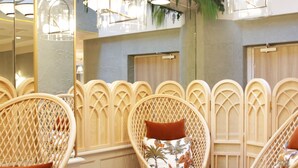 Des chaises et des tables en osier sont disposées dans un coin salon accueillant, agrémenté de lampes suspendues et d’un mur miroitant.