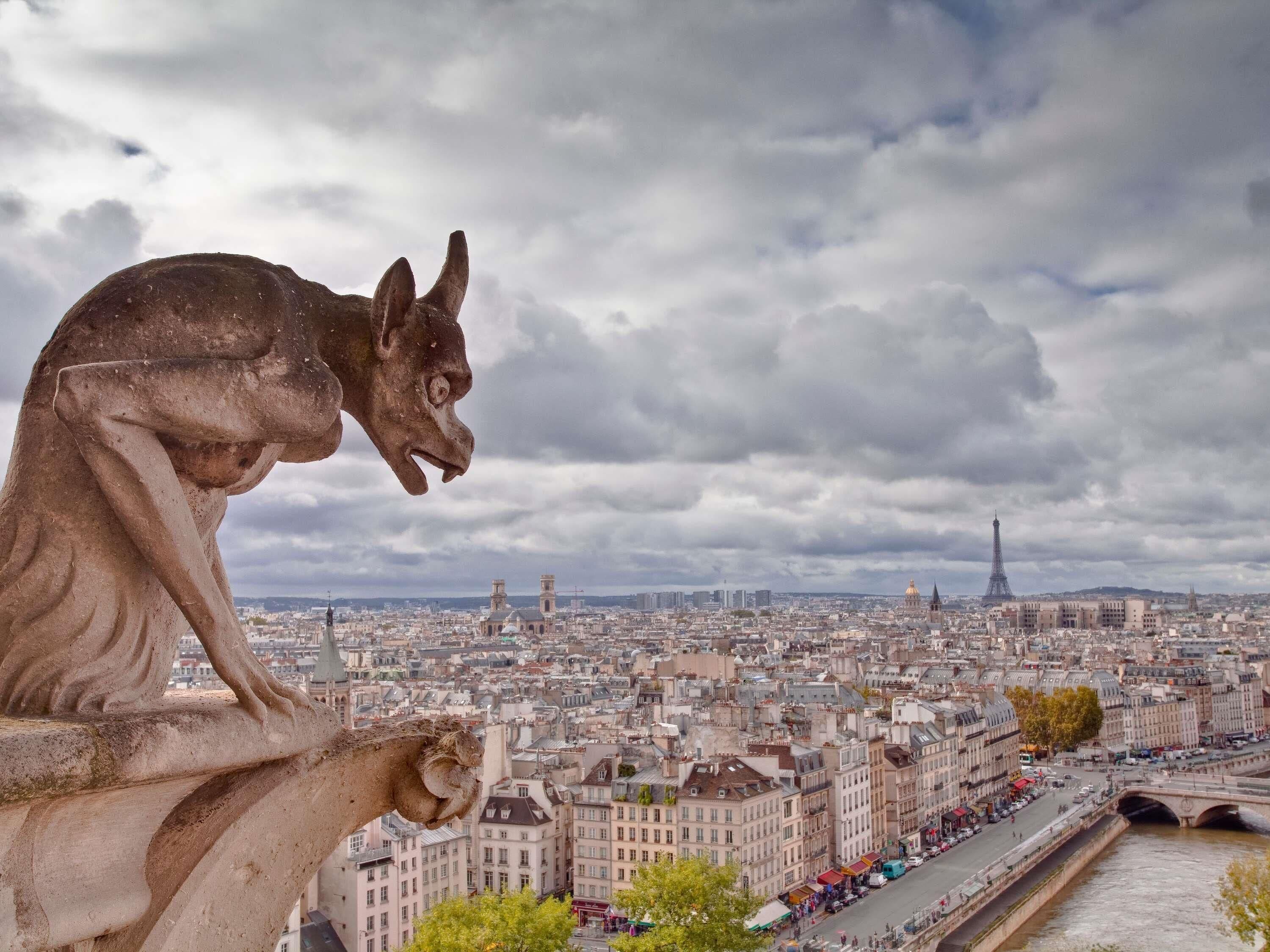 A stone gargoyle overlooking a cityscape with the Eiffel Tower in the distance.