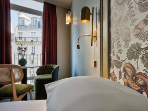 Een hotelkamer met een bed, een stoel, een wandlamp en een raam met gordijnen.
