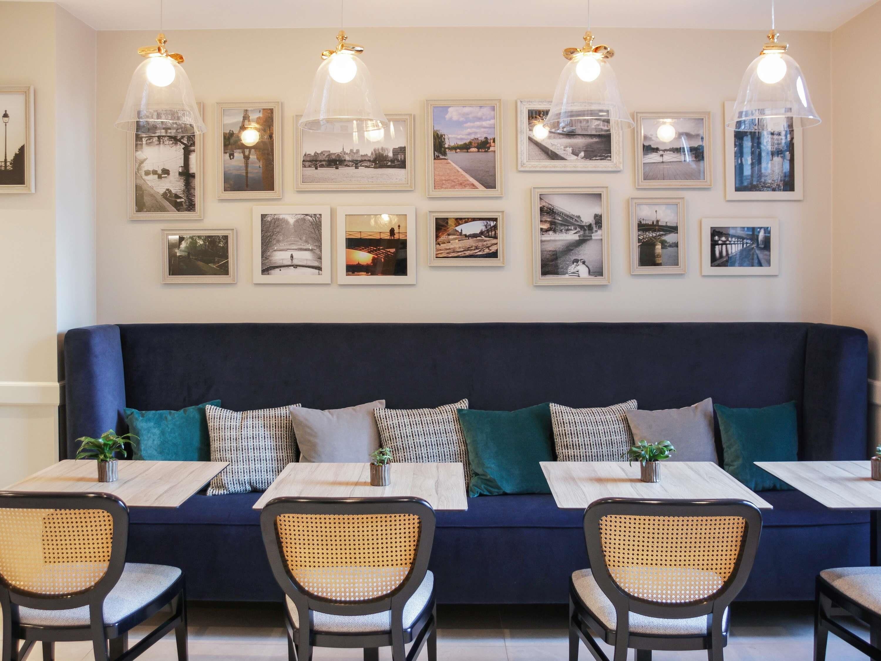 A dining area with a dark blue sofa, wicker chairs, and tables with placemats. There are framed pictures on the wall above the sofa.