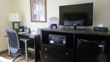 A hotel room with a desk, chair, television, and a small refrigerator.