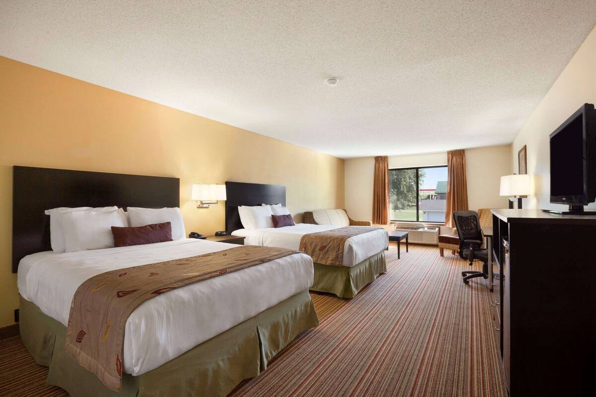 A hotel room with two beds, a desk, a chair, and a television.