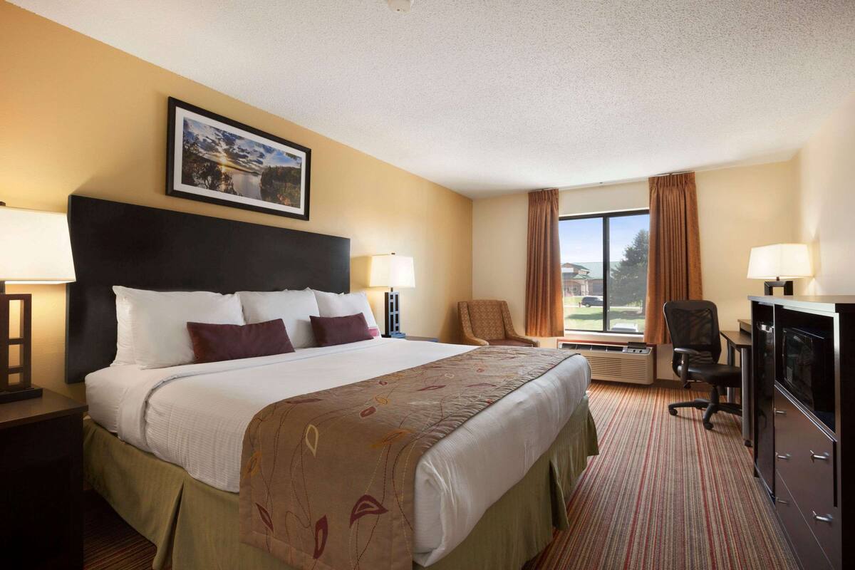 A hotel room with a large bed, two chairs, a desk with a computer, and a window with curtains.