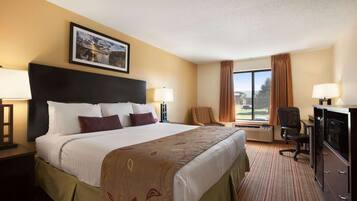 A hotel room with a large bed, two chairs, a desk with a computer, and a window with curtains.