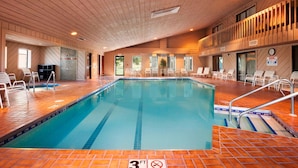 An indoor swimming pool with a wooden ceiling and tiled floor, surrounded by white chairs and a railing. - Ramada by Wyndham Wisconsin Dells (Baraboo)