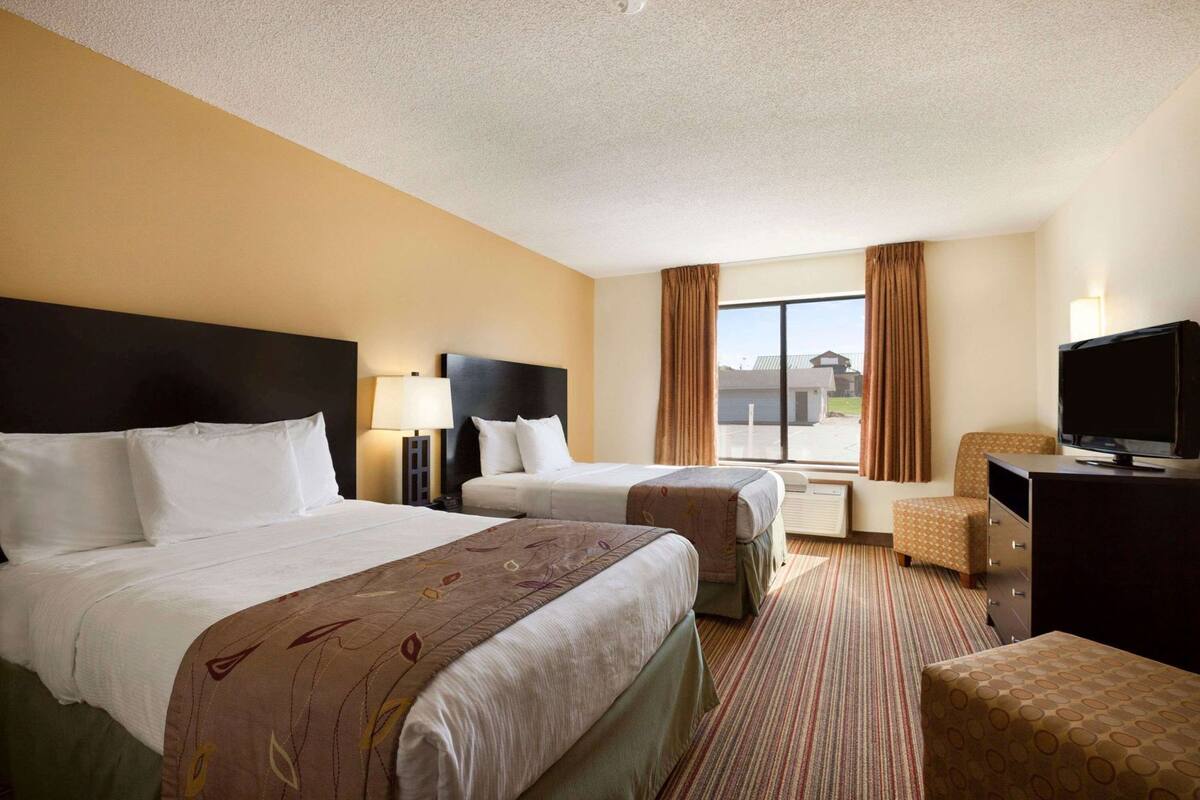 A hotel room with two beds, a TV, a desk, and a window with curtains.