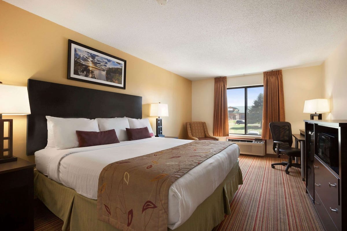A hotel room with a large bed, a desk with a computer, a chair, a TV, and a window with curtains.
