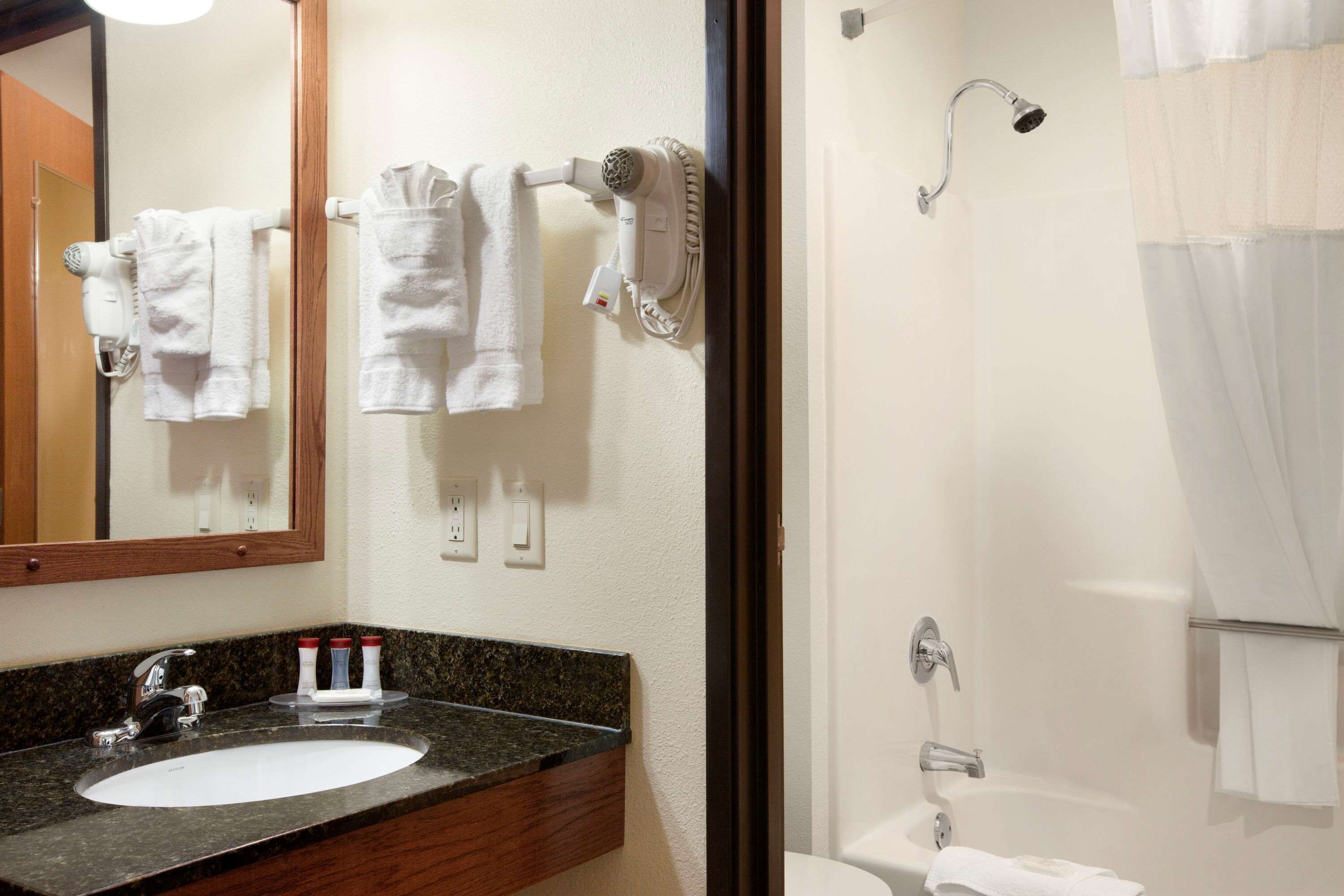 A bathroom with a sink, mirror, towel rack, hair dryer, and shower.