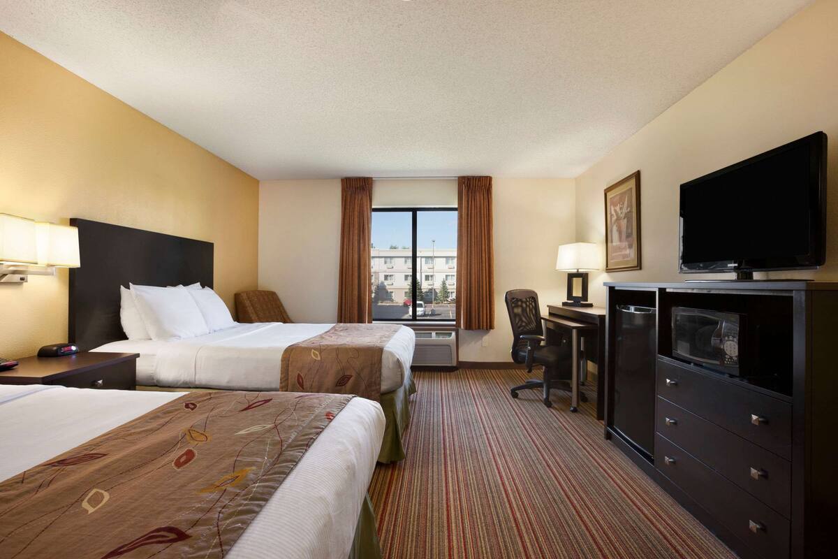 A hotel room with two beds, a desk, a television, and a window with curtains.