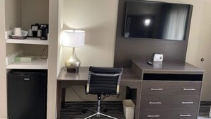 A hotel room with a desk, chair, TV, minibar, and a lamp. - Baymont by Wyndham Topeka (Topeka)