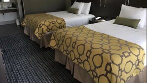A hotel room with two beds, each with a patterned bedspread, a bedside table with a lamp, and a large mirror on the wall. - Baymont by Wyndham Topeka (Topeka)