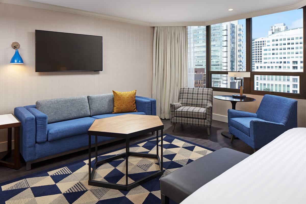 A modern hotel room with a sofa, armchair, and a small table.