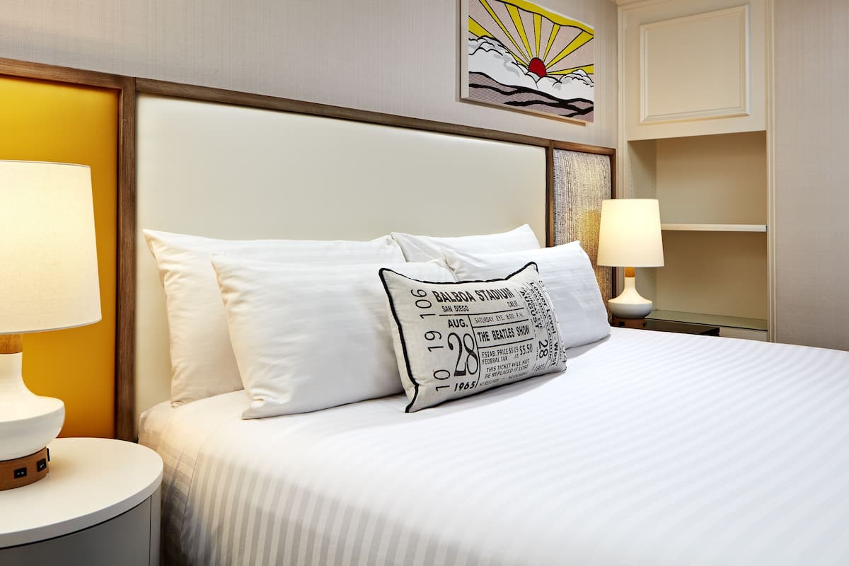 A hotel room with a neatly made bed, a nightstand with a lamp, and a framed artwork on the wall.