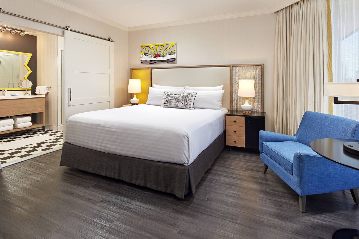 A hotel room with a large bed, a desk with a chair, a mirror, and a painting on the wall.