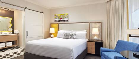 A hotel room with a large bed, a desk with a chair, a mirror, and a painting on the wall.