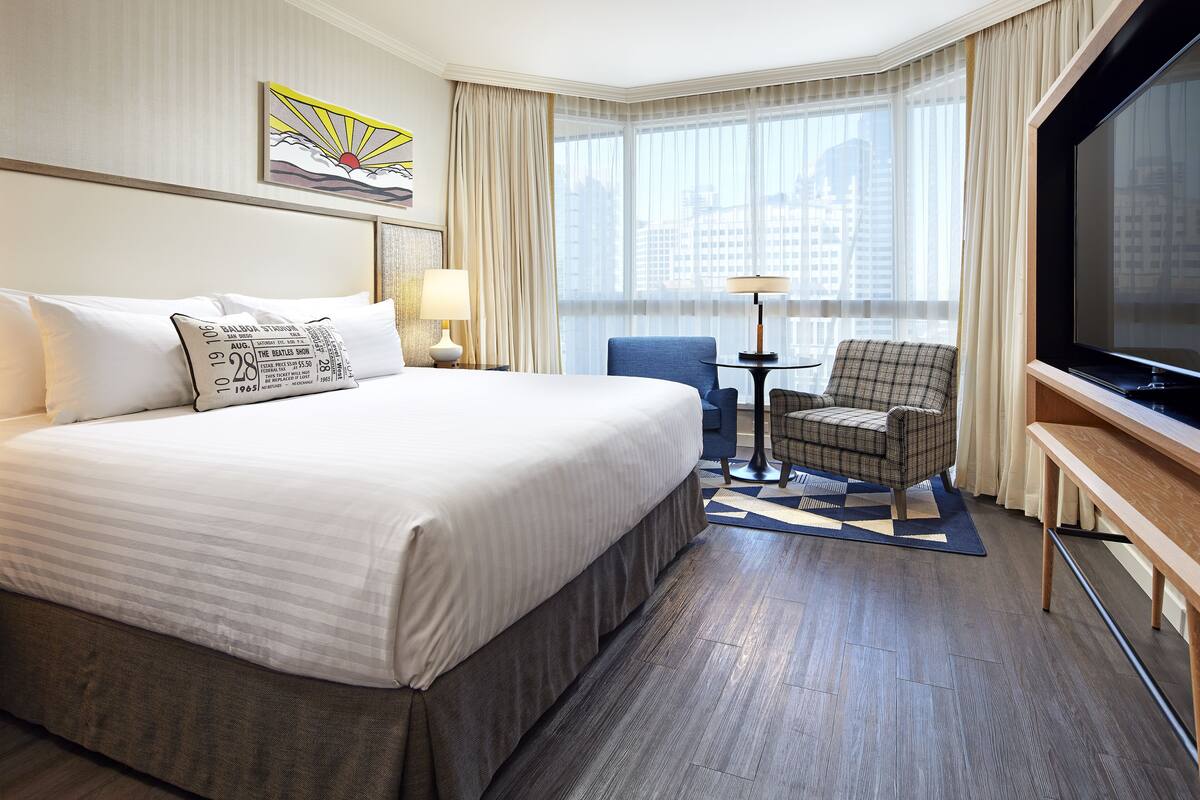 A hotel room with a large bed, a television, a desk, and a chair.