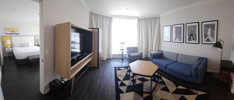 A hotel room with a bed, a TV, a sofa, a small table, and a patterned rug.