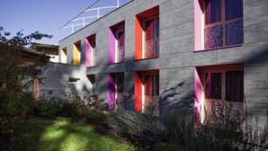 A modern building with multiple windows and balconies, surrounded by a well-maintained garden. - Mercure Bourg En Bresse (Bourg-en-Bresse)