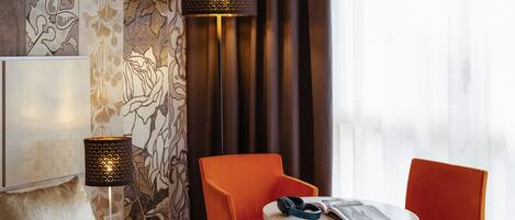 Une chambre d’hôtel avec un lit, deux fauteuils orange, une petite table et deux lampes.