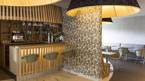 A bar area with stools, a counter, and shelves with bottles and glasses. - Mercure Bourg En Bresse (Bourg-en-Bresse)