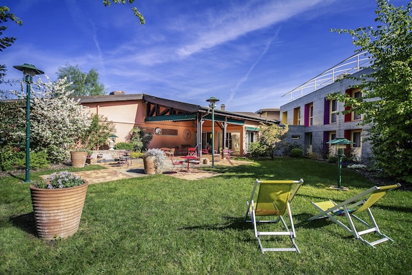 A courtyard with a lawn, outdoor furniture, and a building with a covered patio area.