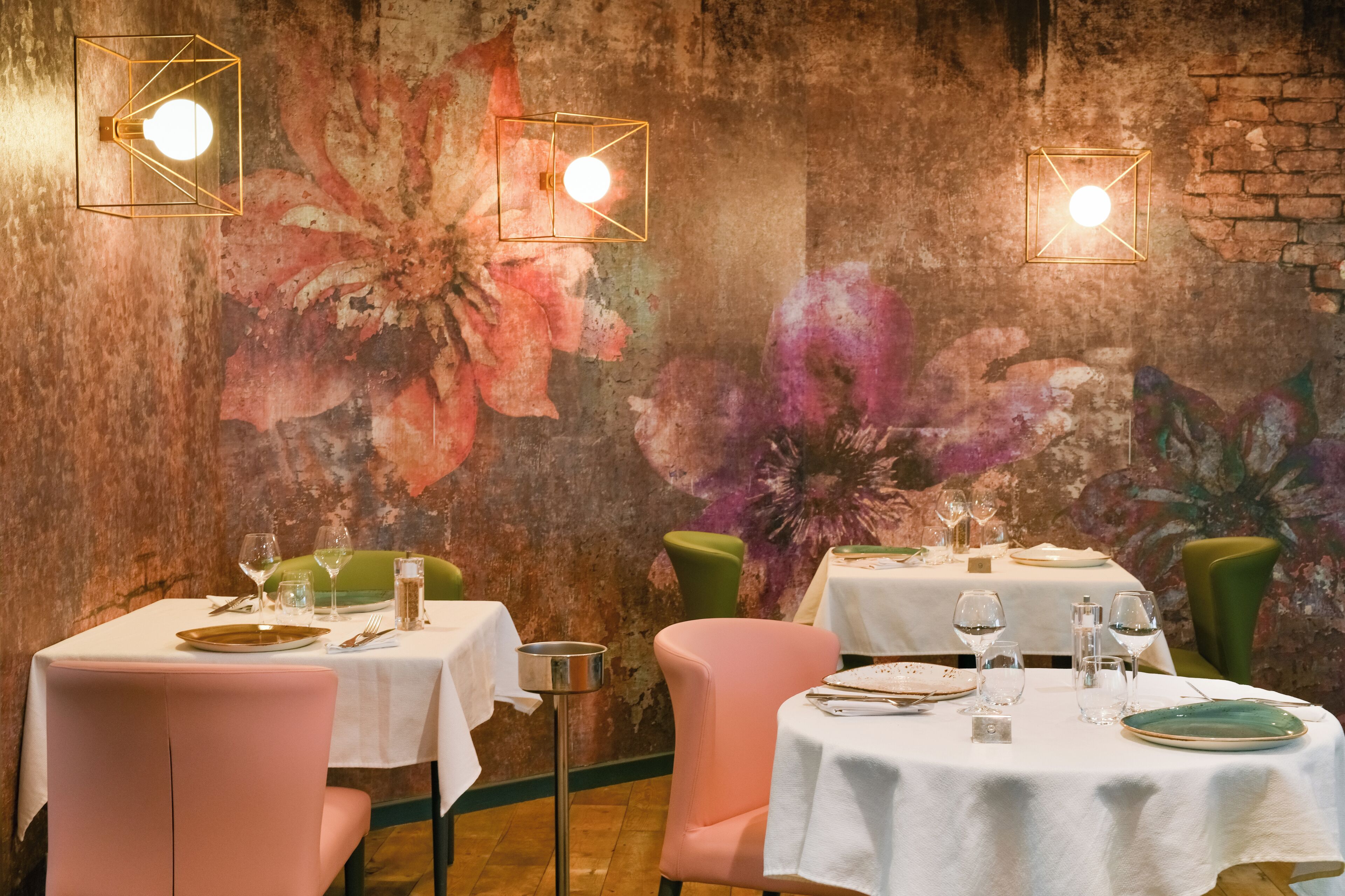 Un comedor con mesas dispuestas para dos, cada una con mantel blanco, sillas verdes y un candelabro.