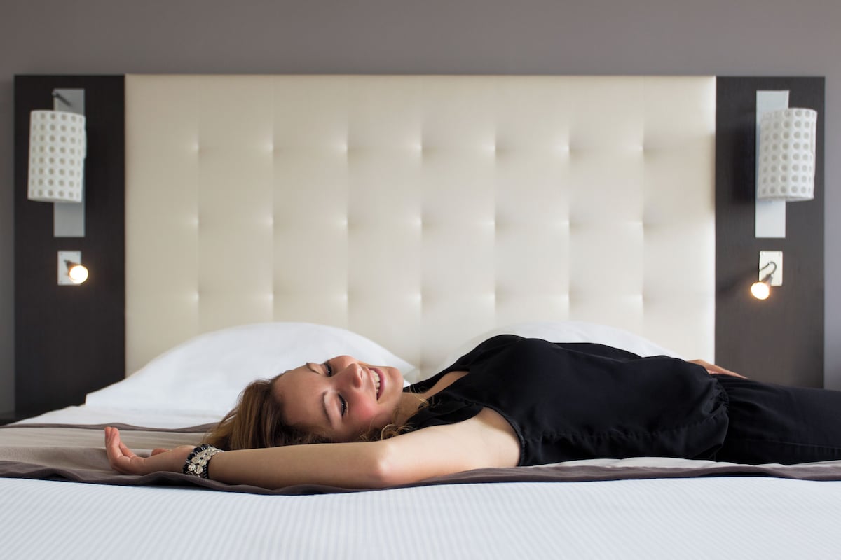 A bed with a tufted headboard, a white pillow, and two wall-mounted light fixtures.