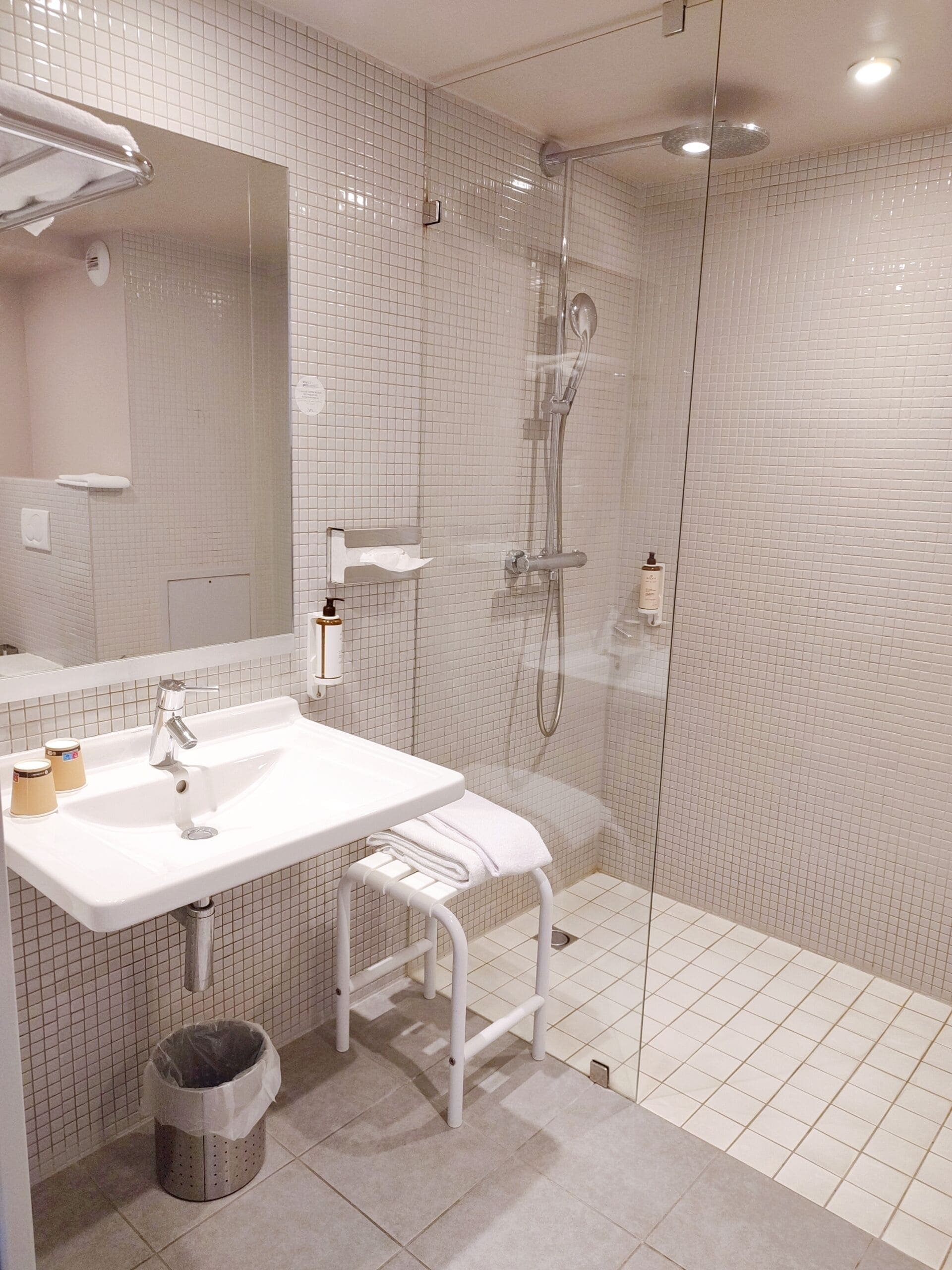 A modern bathroom with a white sink, mirror, and glass-enclosed shower.