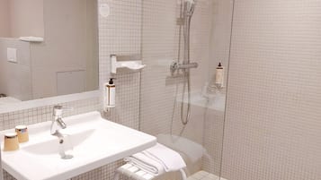 A modern bathroom with a white sink, mirror, and glass-enclosed shower.