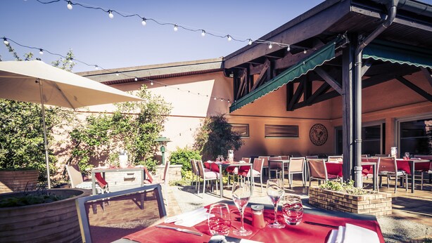 An outdoor dining area with tables set for two, string lights overhead, and a brick planter in the center. - Mercure Bourg En Bresse (Bourg-en-Bresse)