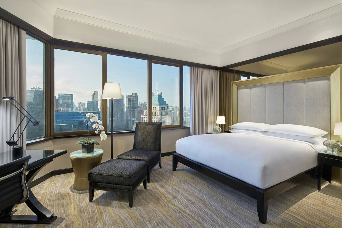 A hotel room with a large bed, a desk, a chair, and a view of the cityscape.