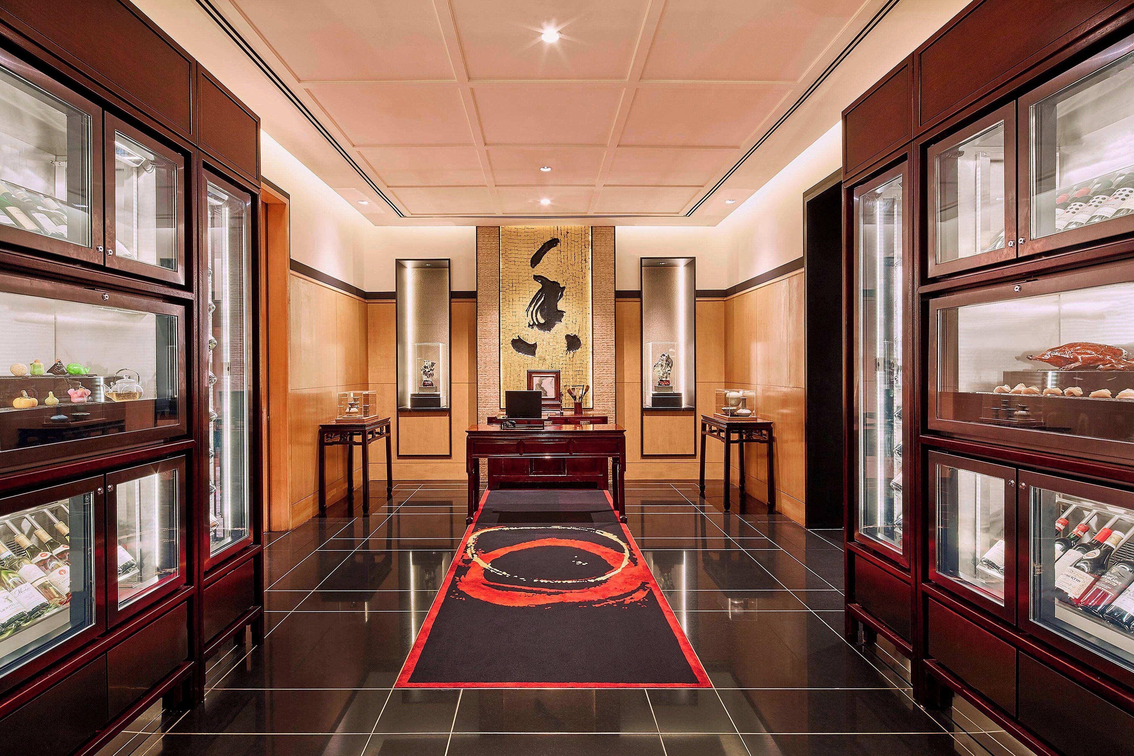 Un hall de hotel con un mostrador de recepción central, vitrinas de cristal y una alfombra decorativa.